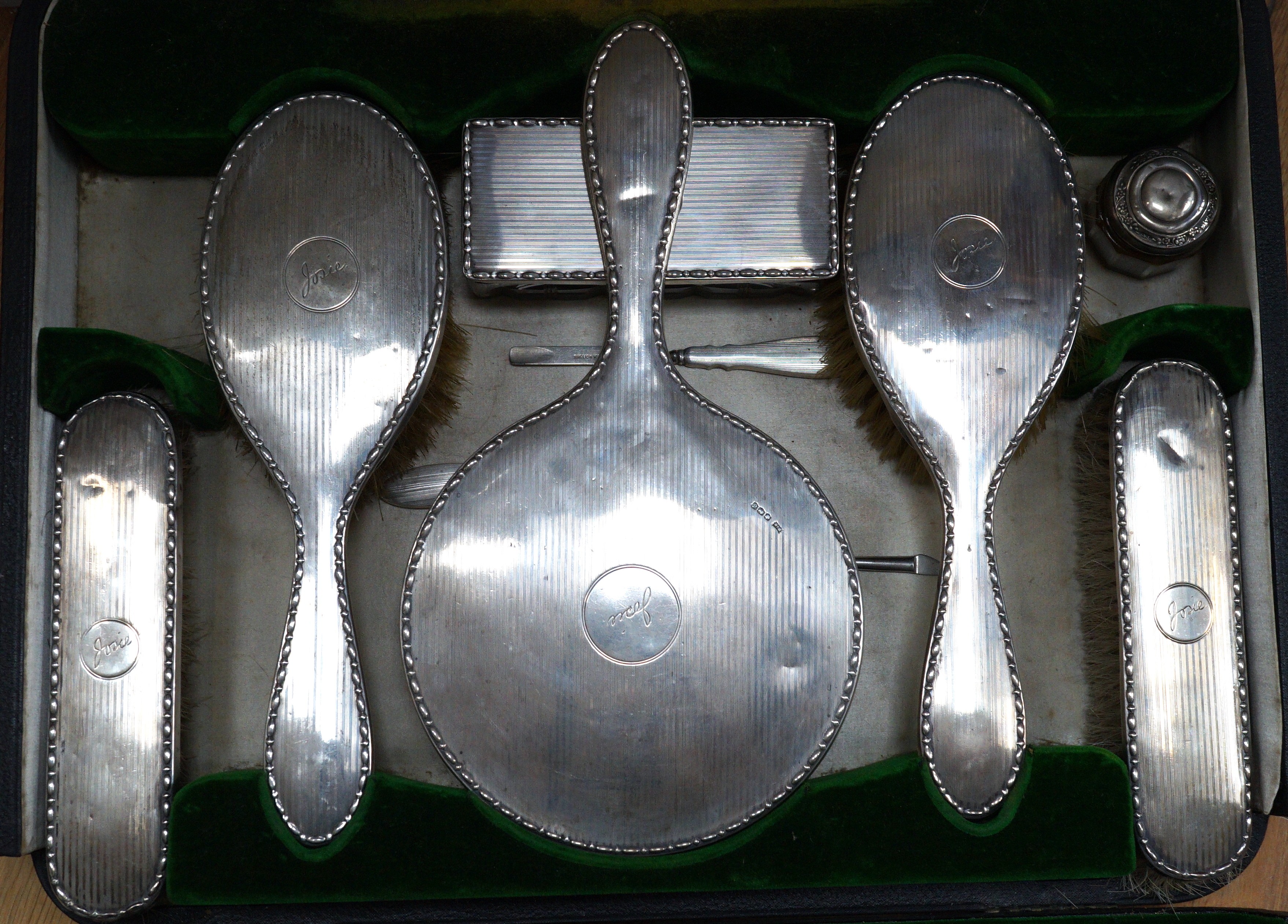 A cased George V silver mounted silver eight piece dressing table set, including tray, mirror and mounted glass tidy, Walker & Hall, Sheffield, 1921, together with four associated silver mounted nail implements, a nail b